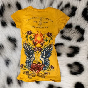 Fin gul t-shirt från Christian Audigier - Snygg gul t-shirt med coola tryck på framsidan och baksidan❤️har en likadan fast röd som jag även säljer😊 det står den är storlek L men skulle säja den liknar mer en M❤️