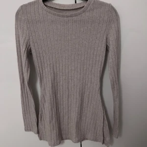 Beige ribbad tröja - Säljer en stilren beige ribbad tröja med långärmad design. Perfekt för kyligare dagar och enkel att matcha med olika outfits. Tröjan har en rund halsringning och är gjord i ett mjukt material.