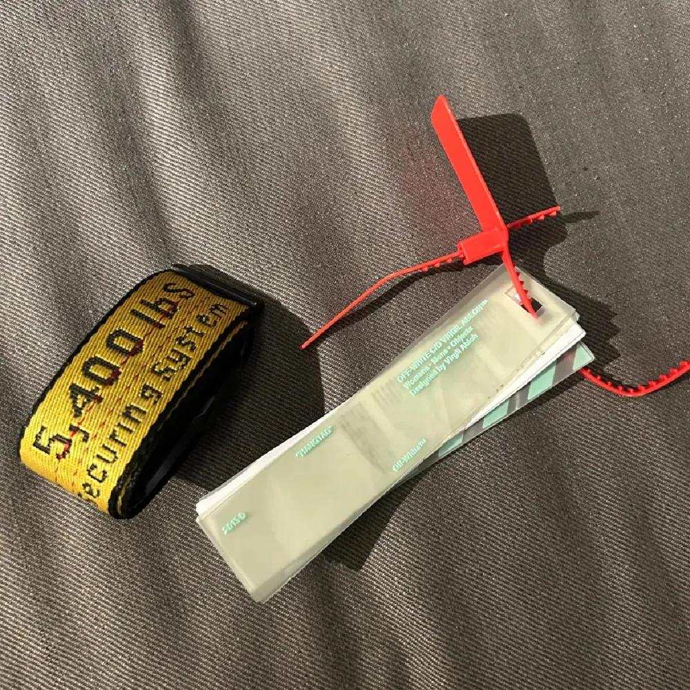 Säljer ett coolt gult bälte från Off-White med svart text och en robust spänne. Bältet har en industriell design med märkets logga och viktkapacitet tryckt längs hela längden. Perfekt för att ge din outfit en edgy touch.. Asusteet.