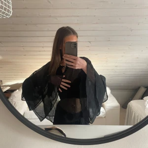 Svart blus från Luzabelle - Snygg svart blus från Luzabelle med vida ärmar och volangdetaljer. Perfekt för en elegant look med en touch av dramatik. Tillverkad i ett lätt och luftigt material.