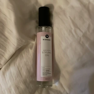 HH Simonsen Styling Oil - Säljer en stylingolja från HH Simonsen. Flaskan rymmer 100 ml och har en stilren design med svart lock och rosa etikett. Perfekt för att ge håret glans och mjukhet.