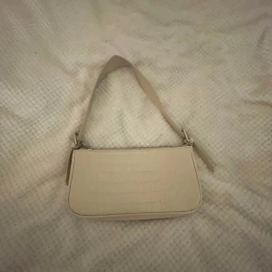 Beige axelväska med krokodilmönster - Snygg beige axelväska med krokodilmönster och dragkedja. Perfekt för att ge din outfit en stilren touch. Väskan har en enkel design med ett justerbart axelband.