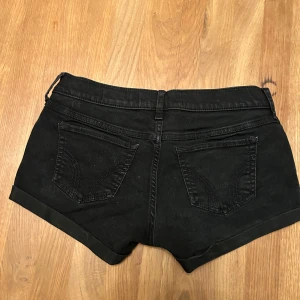 Svarta lågmidjade shorts från Hollister - Snygga svarta lågmidjade shorts från Hollister. Perfekta för en avslappnad stil med klassiska femficksdetaljer och knappstängning. Passar utmärkt för varma sommardagar.