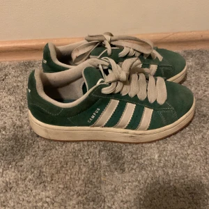 Gröna Adidas Campus sneakers - Säljer ett par gröna Adidas Campus sneakers i mocka med vita detaljer och snörning. Perfekta för en avslappnad stil. Tyvärr för små för mig men super snygga (kan skicka nya skosnören i grönt)💚💚