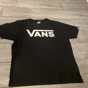 Svart t-shirt från Vans - Säljer en klassisk svart t-shirt från Vans med stort vitt logotryck på bröstet. T-shirten är kortärmad och har en rund halsringning. Perfekt för en avslappnad stil.