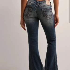 True Religion jeans - Snygga blå bootcut jeans från True Religion med snygga röda detaljer på sömmarna. Säljer pågrund utav att de är för korta för mig. Storlek W24. Aldrig använt. Nypris; 1399kr