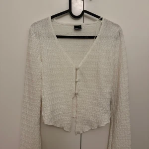 Vit ribbad kofta med knappar - Säljer en söt vit kofta med ribbad textur och knappar framtill. Den har en v-ringad design och långa ärmar, perfekt för lager-på-lager-stil. Passar till både vardag och mer uppklädda tillfällen.