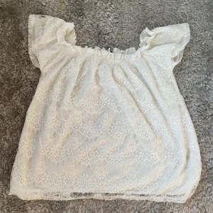 Vit spetsblus - Charmig vit blus i spets med offshoulder-design och korta ärmar. Perfekt för en somrig look med sin luftiga och romantiska stil. Från Gina i storlek M, men passar även S!
