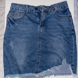Jeanskjol från Amisu - Snygg jeanskjol från Amisu i klassisk blå denim. Kjolen har en rå kant nertill och en femficksdesign med knapp och dragkedja framtill. Perfekt för en avslappnad stil.