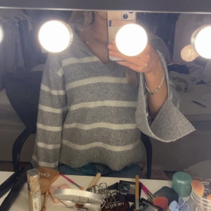 Grå och vit randig tröja från Gina Tricot - Säljer en mysig grå och vit randig tröja från Gina Tricot. Tröjan har en v-ringad hals och långa ärmar, perfekt för kyligare dagar.