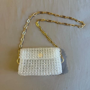 Glittrig axelväska med guldkedja - Snygg glittrig axelväska med en unik design av genomskinliga pärlor. Väskan har en elegant guldkedja som axelrem och stängs med en magnetknapp. Perfekt för att ge en touch av glamour till din outfit.