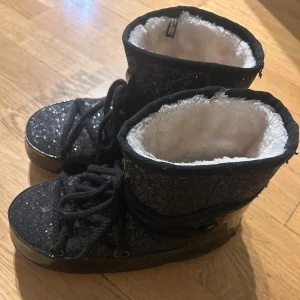 Inuikii liknande skor - Snygga svarta boots med glittrig yta och mjukt vitt foder. Skorna har snörning och en robust sula, perfekt för kyligare dagar. Storlek 40. Använda en gång, superbra skick