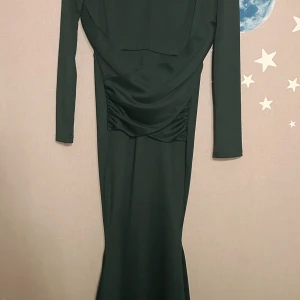 Grön långklänning  - Elegant grön långklänning från SHEIN i sammet med v-ringad design och långa ärmar. Perfekt för en glamorös kväll med sin figurnära passform och omlott-detalj framtill.