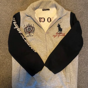 Grå och svart hoodie från Ralph lauren - Säljer en snygg grå och svart hoodie från Polo Club med dragkedja. Den har broderade detaljer på bröstet och ärmarna, samt texten 'Polo Club' på ryggen. Perfekt skick utan skador ✅⚡️