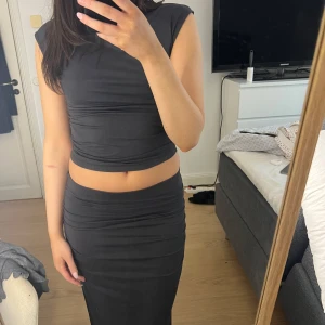 Svart ärmlös tröja och kjol set - Snygg Ish svart ärmlös tröja och kjol med tight passform. Setet har en stilren design och är perfekt för en kväll ute. Den är gjord i ett mjukt och stretchigt material som ger en bekväm känsla.