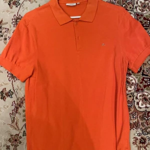 Orange pikétröja från J.Lindeberg - Snygg orange pikétröja från J.Lindeberg i storlek M. Tröjan har korta ärmar och en klassisk krage med knappar. Perfekt för en stilren och avslappnad look. Chill piké