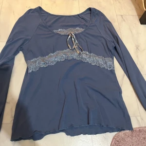 Blå långärmad topp med spetsdetaljer - Säljer en blå långärmad topp med spetsdetaljer och knytning framtill. Perfekt för en stilren och elegant look. Toppen har en rund halsringning och är tillverkad i ett mjukt material.