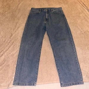 Baggy Carhartt Jeans - Säljer ett par klassiska blå jeans från Carhartt. De har en rak passform och är tillverkade i slitstarkt denim. Byxorna har en knappgylf och fem fickor, med Carhartt-loggan på bakfickan.