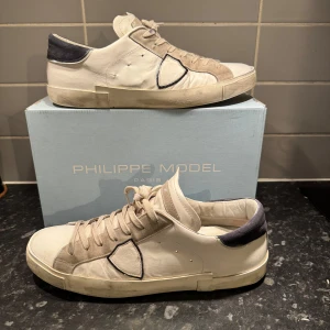 Vita sneakers från Philippe Model - Snygga vita sneakers från Philippe Model med grå detaljer och snörning. Skorna har en stilren design med en kontrasterande mörk häl. Perfekta för en avslappnad och trendig look. Övgör skickat själv så inga fel kan förekomma mvh Jonas😁 har kvitto och allt Og