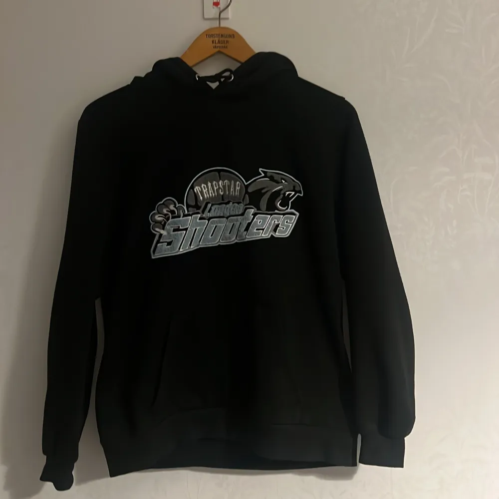 Säljer en svart hoodie från Trapstar med ett coolt tryck av 'London Shooters' och en panter på framsidan. Har en väldigt bra passform den är också i bra skick. Hoodien har en klassisk passform med långa ärmar och en bekväm huva med dragsko.. Neuletakit & Villapaidat.