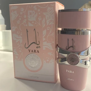 Yara Eau de Parfum från Lattafa - Elegant parfymflaska i ljusrosa med silverdetaljer från Lattafa. Doften Yara kommer i en stilren flaska med ett dekorativt mönster och en matchande kartong. Perfekt för den som söker en sofistikerad och modern doftupplevelse.