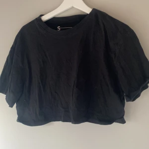 Svart croppad t-shirt - Säljer en svart croppad t-shirt med korta ärmar. Perfekt för en avslappnad stil. Passar bra till jeans eller kjol. Hör av dig vid intresse!