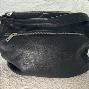 Svart skinnväska från DKNY i mycket fint skick - Snygg svart skinnväska från DKNY med innerfack. Insidan är fodrad med DKNY-logotypen. Väskan är knappt använd. Dustbag följer med.