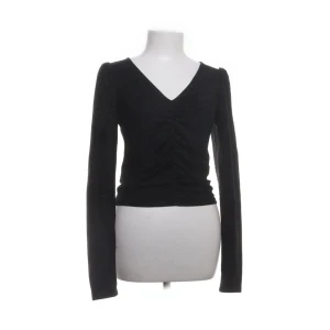 Svart v-ringad tröja - Snygg svart tröja med v-ringning och långa ärmar. Tröjan har en åtsittande passform och rynkdetaljer framtill som ger en stilren look. Glittrig passar till fest och vardag