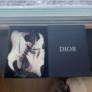 sneakers i vitt och rosa - Snygga sneakers i vitt med svarta och rosa detaljer. Skorna har en chunky sula och snörning framtill. Perfekta för en trendig look.