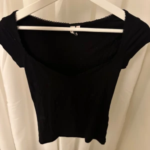 Svart topp från Nelly - Snygg svart topp från Nelly med spetsdetaljer vid halsringningen. Toppen har en tight passform och korta ärmar.