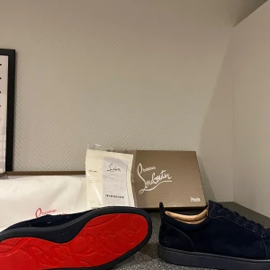  Christian Louboutin - Snygga mörk blåa sneakers från Christian Louboutin med den ikoniska röda sulan. Skorna har en stilren design med snörning och är tillverkade i mocka. Perfekta för den som vill ha en lyxig touch i vardagen. Allt på bild fås med kvitto med mera skorna är i 8/10 i skick priset kan diskuteras vid snabb och smidig affär 