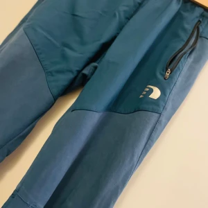 Blå träningsbyxor från Newline - Snygga blå träningsbyxor från Newline med elastisk midja och dragkedjor vid fickorna. Perfekta för en aktiv livsstil med en bekväm passform.