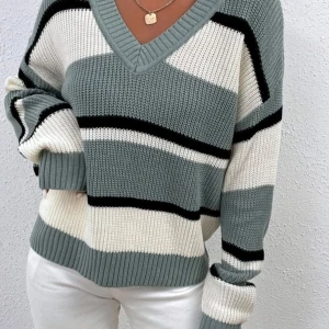 Randig stickad tröja i gråblått och vitt - Säljer en mysig stickad tröja med breda ränder i gåblått, vitt och svart. Tröjan har en v-ringad hals och långa ärmar, perfekt för kyliga dagar. Den är både stilren och bekväm.