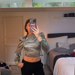 Grön satinblus med öppen rygg - Snygg grön satinblus med långa ärmar och en trendig öppen rygg. Blusen har en knytning bak som ger en elegant touch. Perfekt till fest eller middag !