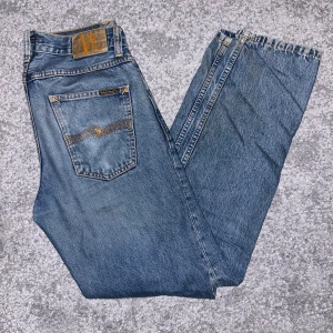 Blå jeans från Nudie - Snygga blå jeans från Nudie med klassisk femficksdesign och orange sömmar. De har en rak passform och är tillverkade i slitstarkt denim. Perfekta för en avslappnad stil.