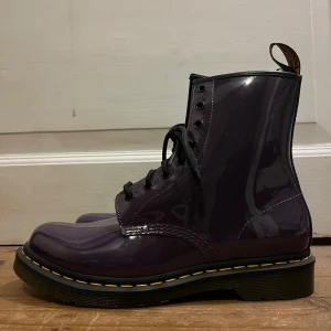 Dr martens  - Oanvända lila Dr. Martens i storlek 42 (normal i storleken). Gula sömmar, en skriptad AirWair-hälögla och en tålig, luftdämpad sula. Modell: 1460 PATENT-LACKLÄDER SNÖRKÄNGOR Material: PU belagt läder. Går inte att köpa nya längre! Torkar lätt bort smuts med fuktig trasa. Fina och coola! Skriv om du undrar något:)