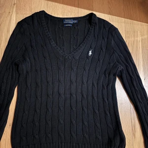 Svart stickad tröja från Polo Ralph Lauren - Säljer en stilren svart stickad tröja från Polo Ralph Lauren i pima-bomull. Tröjan har en v-ringad hals och det klassiska logotypbroderiet på bröstet. Perfekt för en elegant och avslappnad look.