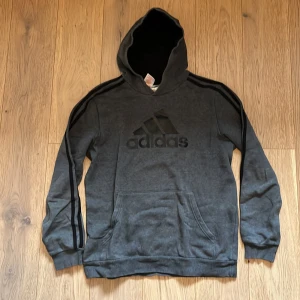 Grå hoodie från Adidas - Säljer en snygg grå hoodie från Adidas med det klassiska logotypen på bröstet. Tröjan har långa ärmar och en praktisk magficka. Perfekt för en avslappnad stil. Köptes för 440kr säljs för 340kr