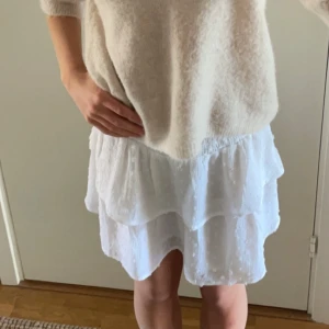 Vit volangkjol - Säljer en söt vit volangkjol med flera lager som ger en luftig och romantisk känsla. Perfekt för varma sommardagar eller en avslappnad vårlook. Kjolen har en elastisk midja för bekväm passform.