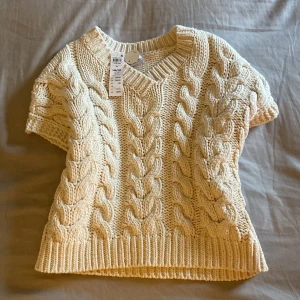 Beige stickad tröja  - Säljer en mysig beige stickad tröja från Lindex med flätstickat mönster. Tröjan har en v-ringad hals och korta ärmar, perfekt för lager på lager-stil. Passar både till jeans och kjol.💓lappen är kvar! Aldrig använd bara testad passar Xs och s