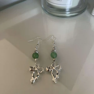 Silverörhängen med gröna pärlor och rosett - Säljer ett par eleganta silverörhängen med gröna pärlor och en fin rosettdetalj. Perfekta för att ge en touch av stil till vilken outfit som helst. Passar både till vardag och fest!