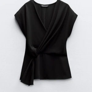 Svart omlottopp från Zara - Snygg svart omlottopp från zara. Toppen har en knytning på sidan som ger en fin detalj och en v-ringad hals. Perfekt för både vardag och fest! Aldrig använd/testad, lapp finns kvar ❤️ 