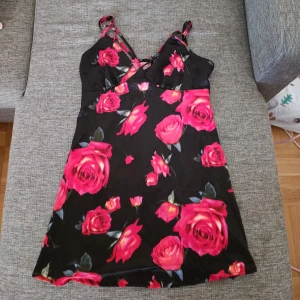 Svart blommig klänning från Wild Fable - Säljer en svart klänning från Wild Fable med stora röda rosor. Den har smala axelband och en v-ringad design. Perfekt för en sommarren ❤️🌹 obs betalning sker via swish 