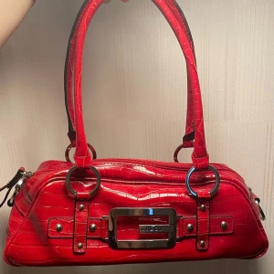 Röd Guess väska - Jättesnygg röd Guess väska. Knappt använd därav i väldigt fint skick. Säljer då min mamma ej använder den. Liten i storleken, rektangel formad. Får enkelt plats med mobil, nycklar, plånbok och annat smått.  En riktig dröm väska 