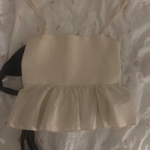 Beige topp med svart rosett - Söt beige topp med svart rosett som man knyter baktill. Använd sparsamt! Från Zara 