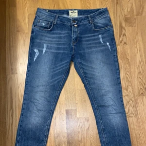 Blå jeans från Morris - Snygga blå jeans från Morris med slitna detaljer och klassisk femficksdesign. Jeansen har en normal passform och är tillverkade i ett robust denimtyg. Perfekta för en avslappnad stil. Skulle säga att den skulle passa runt någon 165-174 cm