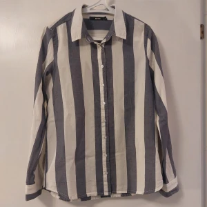 Randig skjorta från Bik Bok - Snygg randig skjorta från Bik Bok i storlek XS. Skjortan har breda vertikala ränder i vitt och blått med knappar framtill. Perfekt för en stilren look. Sitter mer som en M