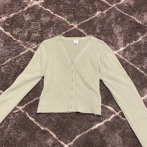 Ljusgrön ribbad kofta från Lindex - Säljer en ljusgrön ribbad kofta från Lindex med knappar framtill. Koftan har en v-ringad design och långa ärmar, perfekt för en stilren look. Passar bra till både jeans och kjol. 🌿