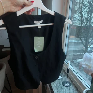Svart väst med knappar - Snygg svart väst med knappar framtill. Perfekt för att lägga till en stilren touch till din outfit. Västen har en klassisk design och är lätt att matcha med olika plagg. 80kr plus frakt 