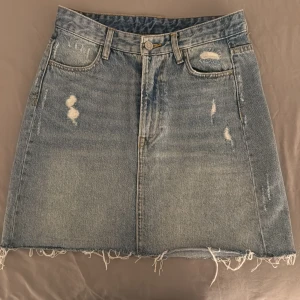 Blå jeanskjol från H&M - Snygg blå jeanskjol från H&M i storlek 34. Kjolen har en fransig nederkant och slitna detaljer både fram och bak. 